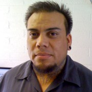 Man with short, spiky dark hair, a goatee, and neck tattoos